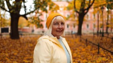 Fall. Cheerful caucasian mature blonde woman smile relaxing resting walking in city park forest alone outdoors. High quality FullHD footage