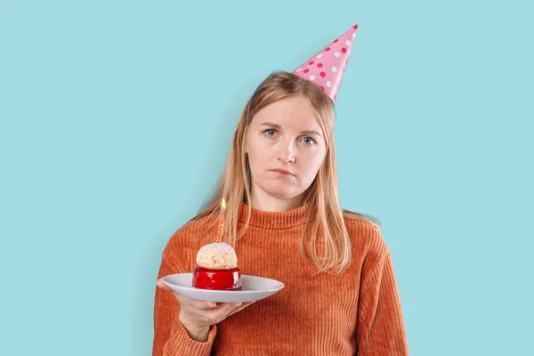 Upset 20s woman smeared with cream after eating festive cake expresses negative emotions as feels lonely celebrates Birthday poses against blue background
