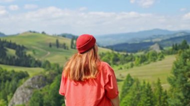 4k Young woman in orange jacket stand up on top of mountain, raises arms into air, happy and drunk on life, youth and happiness. Watching the sunset with beautiful landscape. 