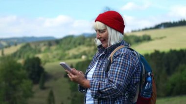 Woman hiker, hiking backpacker traveler camper with her phone camera on the top of mountain in sunny day. Beautiful mountain landscape view. Hiking, backpacking. 4K 