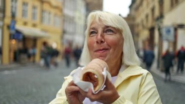 Happy senior 50s woman eats Trdelnik on the street market in Prague, Czech Republic. 