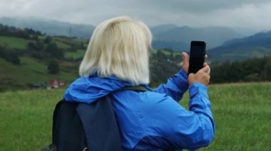 Woman hiker, hiking backpacker traveler camper with her phone camera on the top of mountain in sunny day. Beautiful mountain landscape view. Hiking, backpacking. 4K 
