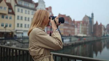 Close up portrait of cheerful beautiful female in good mood with camera standing outdoors in city. Happy pretty young woman tourist taking photo. Photographer taking pictures. Urban concept. 