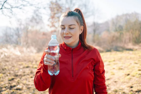 Image of sportswoman drinking water while working out on sports ground