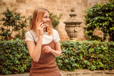 Şehir caddesinde sabahları cep telefonuyla konuşan neşeli sarışın bir kadının yakın plan portresi. 