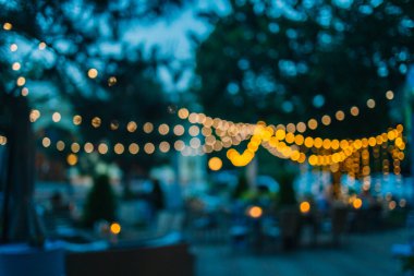 Yaz partisinde restoranda ya da bahçedeki kafede asılı moda dekorasyon iplikçikleri. Açık hava elektrik lambaları. Parlak mavi gökyüzü