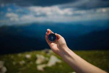 Traveler with compass seeking a right way in the mountains during hike. Navigation concept in explore travel. clipart