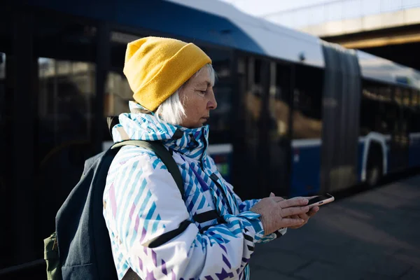 60 'ların yaşlı kadın yolcusu tren tarifesini izliyor ve istasyonda beklerken akıllı telefonuyla tren biletleri alıyor..