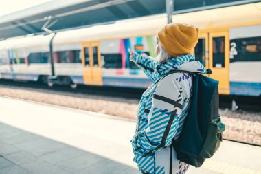 Yürüyüş kıyafetleri içinde sırt çantalı yetişkin bir kadının arka görüntüsü tren istasyonunda dururken gidiş yönünü gösteriyor. Yüksek kalite fotoğraf