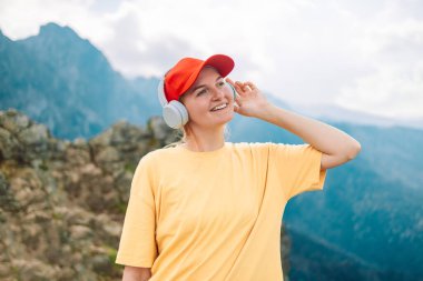 Kulaklıklı kadın doğada ve dağda müzik dinliyor, uzun sarı saçlı kadın turist yürüdükten sonra dinleniyor, yolculuğun tadını çıkarıyor, boşluğu kopyalıyor.