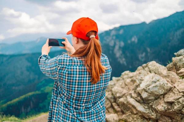 年轻的女人站在山顶上 拿着相机拍照 女人座落在山顶上 身后的风景令人叹为观止 — 图库照片