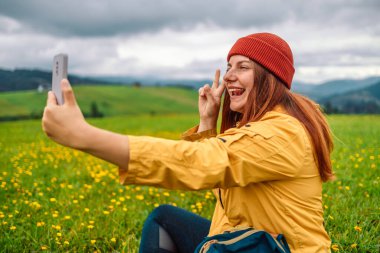 Selfie turisti kadın cep telefonuyla dağ yürüyüşü yaparken selfie çekiyor. Mutlu gülümseyen kız kameraya bakıyor. 