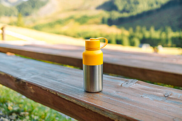 Camping thermos with hot tea, coffee on a wooden bench in a mountain forest. High quality photo