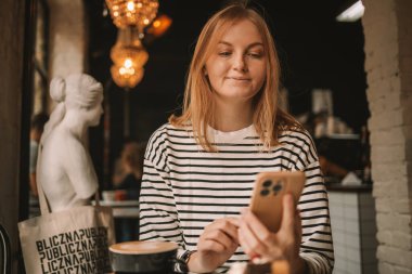 Kafede kahve içerken cep telefonu kullanan mutlu güzel bir kadın. Yüksek kalite fotoğraf