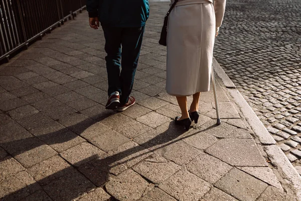 stock image Limping woman with cane and man walking down the street, rear view. Couple together, concept of diseases of the joints and spine