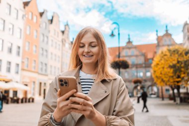 Başarılı bir seyahat blogcusu Gdansk eski kasabasında merkez meydanında yürürken cep telefonu uygulamasında e-posta kutusunu kontrol ediyor. Polonya 'da seyahat. Etkileyici bir kadın şık kıyafetler giyiyor internette sohbet ediyor.