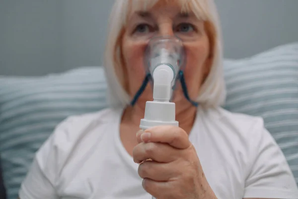 stock image Sick upset caucasian senior woman with an inhaler. Unhealthy female doing inhalation at home, she use nebulizer and inhaler for the treatment, sitting on the couch at home, need treatment. 