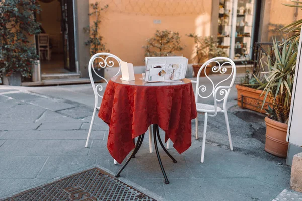stock image Round wooden table with a red holiday tablecloth and cozy white chair at street cafe. Vacant restaurant furniture on the terrace outdoors.Pisa Italy city. High quality photo
