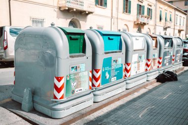Pisa, İtalya - 18 Mart 2023: Çöp tenekelerinin farklı renkleri örgü örülmüş bir çitin arkasında duruyor. Bir Avrupa şehrinde çöpleri ayırmak için çöp konteynırları. Yüksek kalite fotoğraf