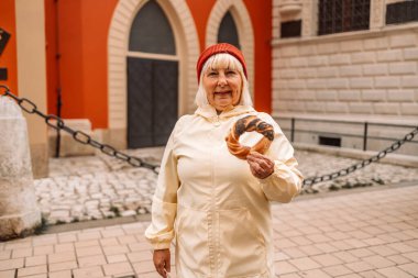Krakow 'daki eski şehir merkezi manzarasına karşı elinde prezel, geleneksel Polonya çerezi tutan yaşlı kadın.. 