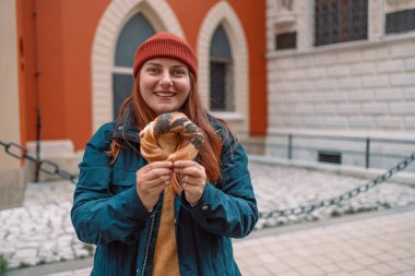 Parlak şapkalı ve sonbahar ceketli bir turist kadın, Krakow 'daki eski şehir meydanında fırında pişirilmiş obwarzanek geleneksel Polonya usulü çerez simidi tutuyor. 