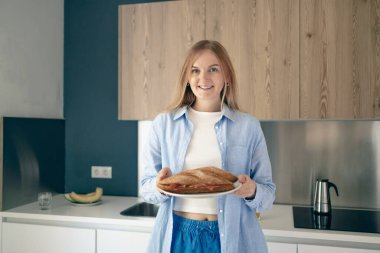 Kadının yakın plan portresi aceleyle taze pişmiş baget ve jambonlu sandviçi sabah kahvaltısı için iç mekan mutfağında yiyor.. 