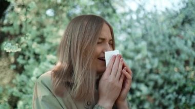 Genç ve güzel bir kadın çiçek açan ağacın önünde hapşırıyor. Bahar alerjisi konsepti. Yüksek kaliteli FullHD görüntüler