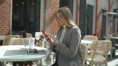 Dışarıda modern akıllı telefon kullanan, kafede kahve içen, sosyal medyayı yakından okuyan çekici, genç, sarışın bir kadının yakın çekimi.
