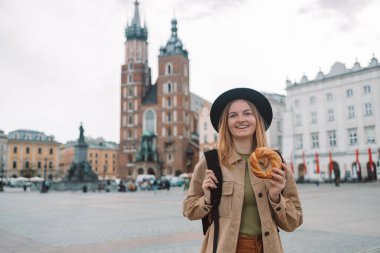 Şık elbiseli ve şapkalı mutlu sarışın bayan turist Krakow 'daki Market Meydanı' nda geleneksel Polonya usulü cips yiyor. Avrupa 'yı gezmek. Aziz Mary Bazilikası