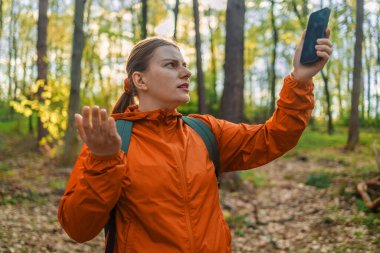 Kızgın kadın turist yürüyüşçüsü elinde akıllı telefon sinyaliyle ormanda arama yapıyor. İletişim, hücresel sorun, kötü bağlantı. Sinyal şebekesi yok. İletişim yok, irtibatı kaybettik.