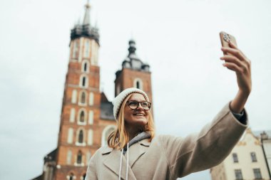Genç sarışın turist Polonya 'nın Krakow kentindeki pazar meydanında cep telefonuyla selfie çekiyor. Yüksek kalite fotoğraf