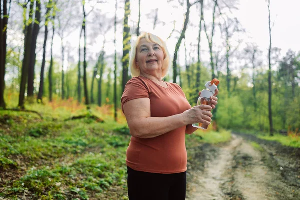 Ormanda şişeden su içen 60 'lı yaşlarda çekici bir kadının portresi. Yüksek kalite fotoğraf