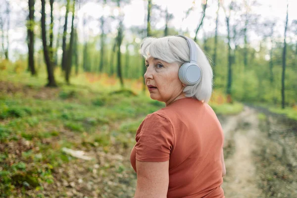 Stock image Fitness, health and a running senior woman on a road through a forest or park for cardio and endurance. Exercise, mockup and workout with a mature female runner or athlete training outdoor in nature