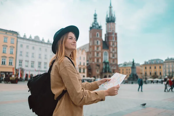 stock image Upset stylish clothes blond girl tourist travels looking for directions on map while traveling through the old town of Krakow in spring, Poland. St. Marys Basilica. High quality photo