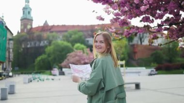 Wawel Kalesi yakınlarındaki Krakow eski kasabasında haritayla gezen genç bir kadın. Sakura Kiraz Çiçeği Sokağı. Baharda kiraz ağacının pembe çiçekleriyle muhteşem manzaralı bir park..