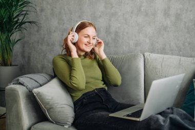 Kulaklıklar, dizüstü bilgisayarlar ve kadın evdeki bir kanepede müzik ya da ses dinlerken çevrimiçi yayınlanıyor. Sakin bir kadın kanepede dinlenip internet bağlantısı ve teknolojisi olan radyo ya da şarkı dinliyor.
