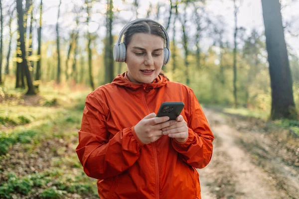 女孩在耳机中听音乐和在手机上打字的肖像 耳机和妇女为了健康 锻炼和健康而在大自然中徒步旅行 — 图库照片