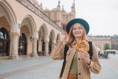 Krakow 'daki pazar meydanında elinde prezel, geleneksel cips taşıyan şık bir kadın turist. Krakow Kumaş Salonu 'nun arka planında kraker tutan bir turist. Yüksek kalite fotoğraf