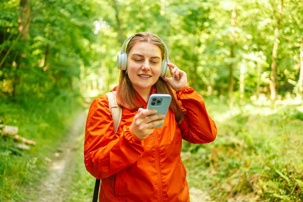 在森林里散步之后 年轻的女人在耳机里听着音乐 在夏夜的阳光下背着背包在森林里休息 高质量的照片 — 图库照片