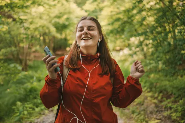 在森林里散步之后 年轻的女人在耳机里听着音乐 在夏夜的阳光下背着背包在森林里休息 高质量的照片 — 图库照片
