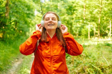 Kulaklıkla müzik dinleyen genç bir kadın ormanda yürüdükten sonra dinleniyor, yaz mevsiminde günbatımında ormanda bir sırt çantası taşıyor. Yüksek kalite fotoğraf