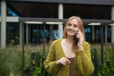 Genç serbest çalışan kadın sokakta yürürken iş telefonuyla konuşuyor. Şehir arka planında dururken elinde cep telefonu tutan çekici bir kadın..