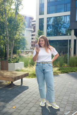 Güneşli şehir caddesinde telefonunu kullanan neşeli genç bir kadın. Yüksek kalite fotoğraf