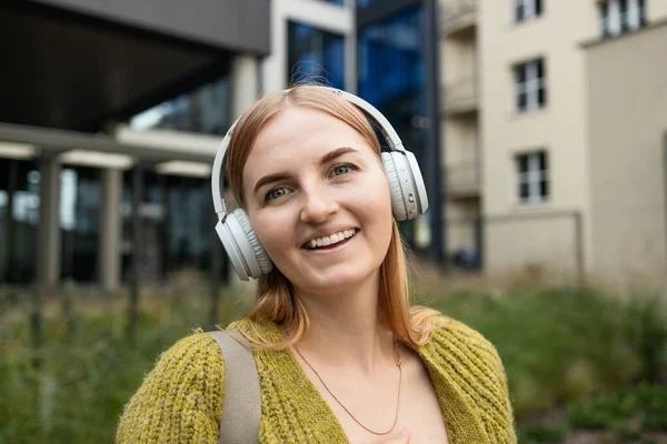 年轻的金发白人女人一边在城市里散步一边听音乐 高质量的照片 — 图库照片