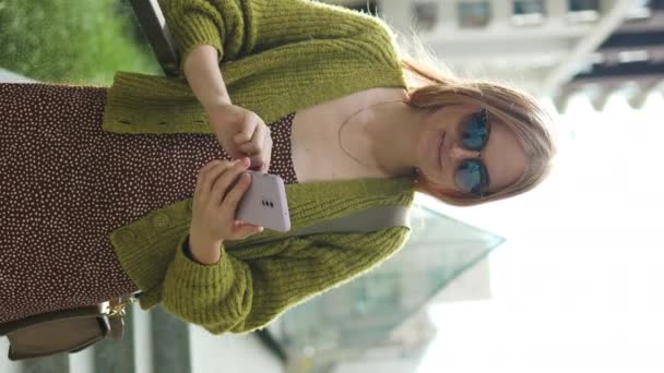 都市の外にサングラスをかけているクールな千年紀のブロンドの女性の写真は 都市の携帯電話を見ています 高品質の写真 — ストック動画