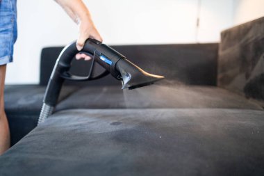 Cleaning service company employee removing dirt from furniture in flat with professional equipment. Female housekeeper arm cleaning sofa with washing vacuum cleaner close up. High quality photo