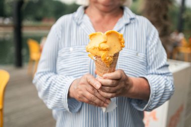 Happy smiling senior woman dressed in stylish clothes eating ice cream in the city summer outdoors cafe interior. High quality photo