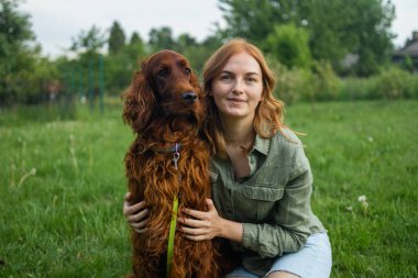 Güzel sarışın, gülümseyen, kot şortlu, mutlu bir kadın camda oturuyor ve yaz parkında günbatımı ışınları tarlasında kızıl, uzun saçlı, sevimli bir köpeği eğitiyor. Evcil hayvan ve hostes