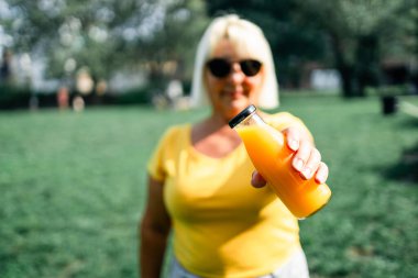 Kırmızı yaz içeceği, meyve suyu ya da yaz parkında meyve suyu olan kadın el ele tutuşma şişesi. Detoks diyet sebze suyu kavramı.