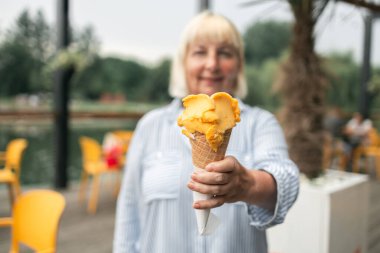 Happy smiling senior woman dressed in stylish clothes eating ice cream in the city summer outdoors cafe interior. High quality photo